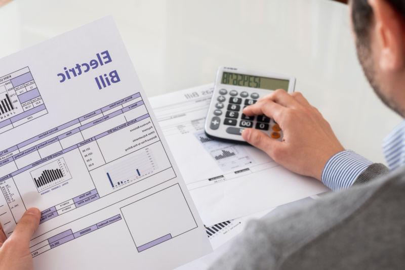 Man sitting at a table with a calculator and paper electric bill